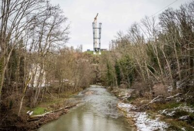 Fluss im Vordergrund, links und rechts Bäume und im Hintergrund der Pylon der Neckarline