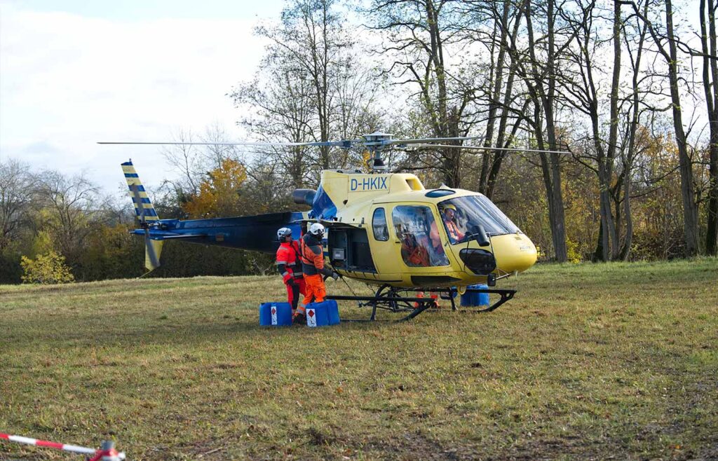Nahansicht auf eines Hubschraubers auf einer Wiese mit einem Piloten und 2 weiteren Personen in Warnanzug