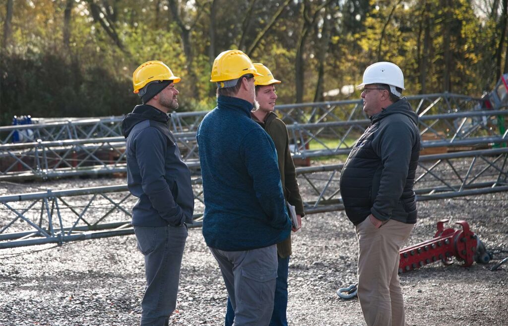 Drei Männer mit Bauhelm vor einer Baustelle