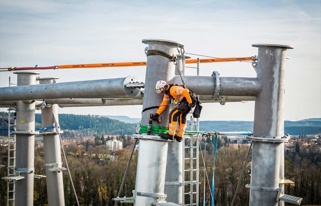 Pylon der Neckarline wird zusammengebaut und ein Arbeiter schraubt mit einem Akkuschrauber