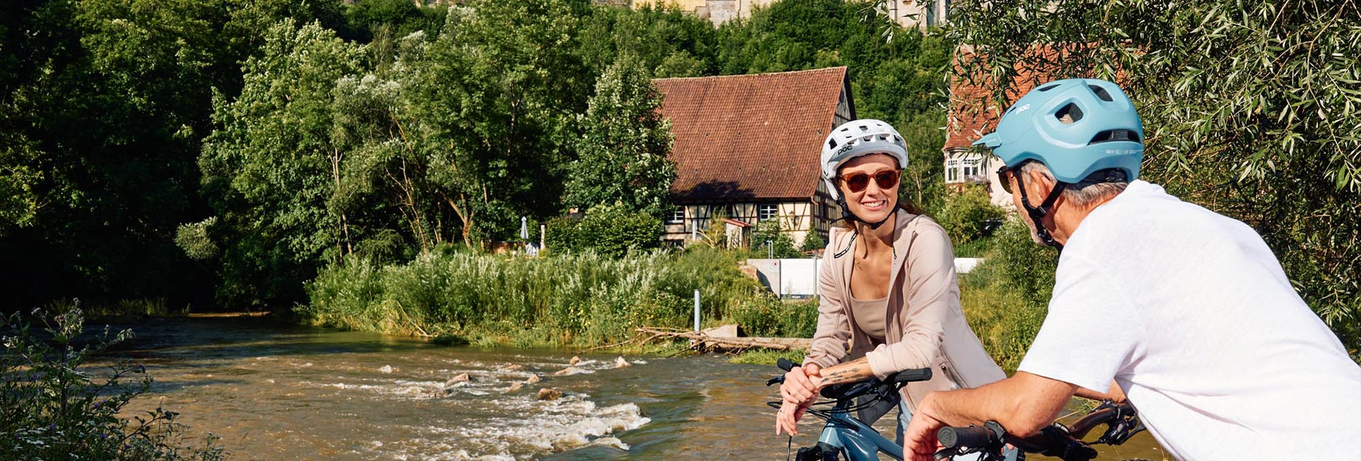 Ein Paar beim Fahrradfahren neben einem Fluss vor zwei historischen Häusern