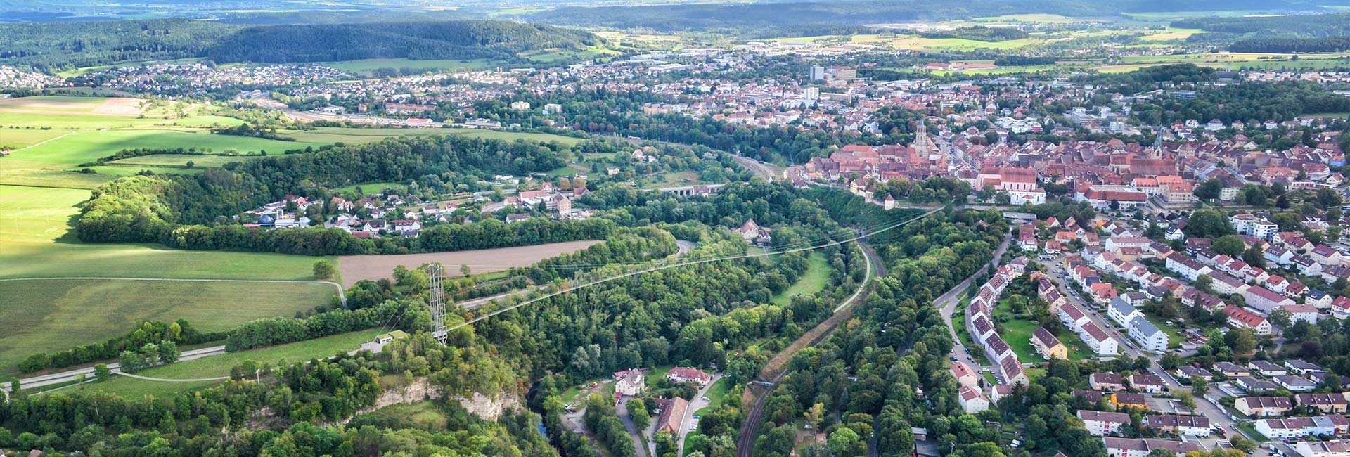 Übersicht über eine Stadt mit Kirchturm und Bergen und grünen Wiesen als Landschaft