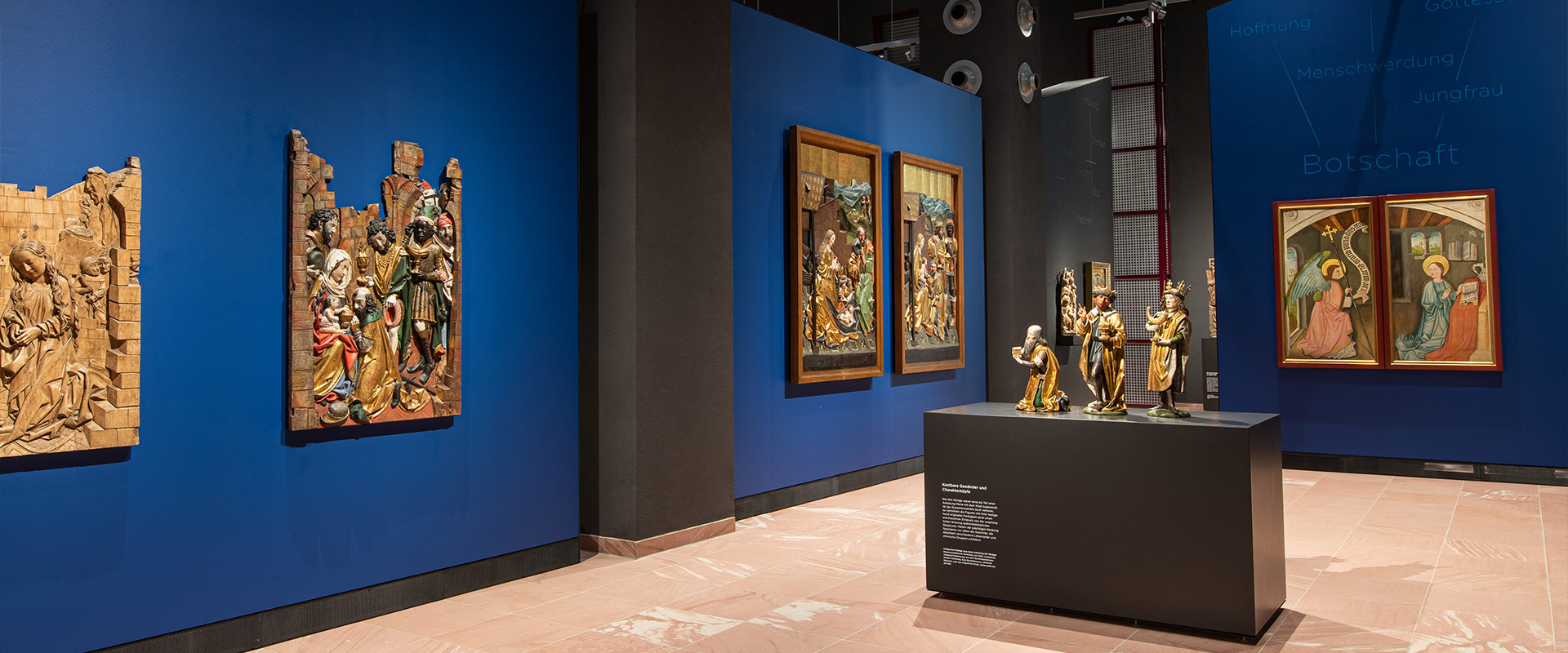 Blick in einen Museumsraum mit christlichen Bildern und Kunst an den blauen Wänden und drei Statuen in der Raummitte