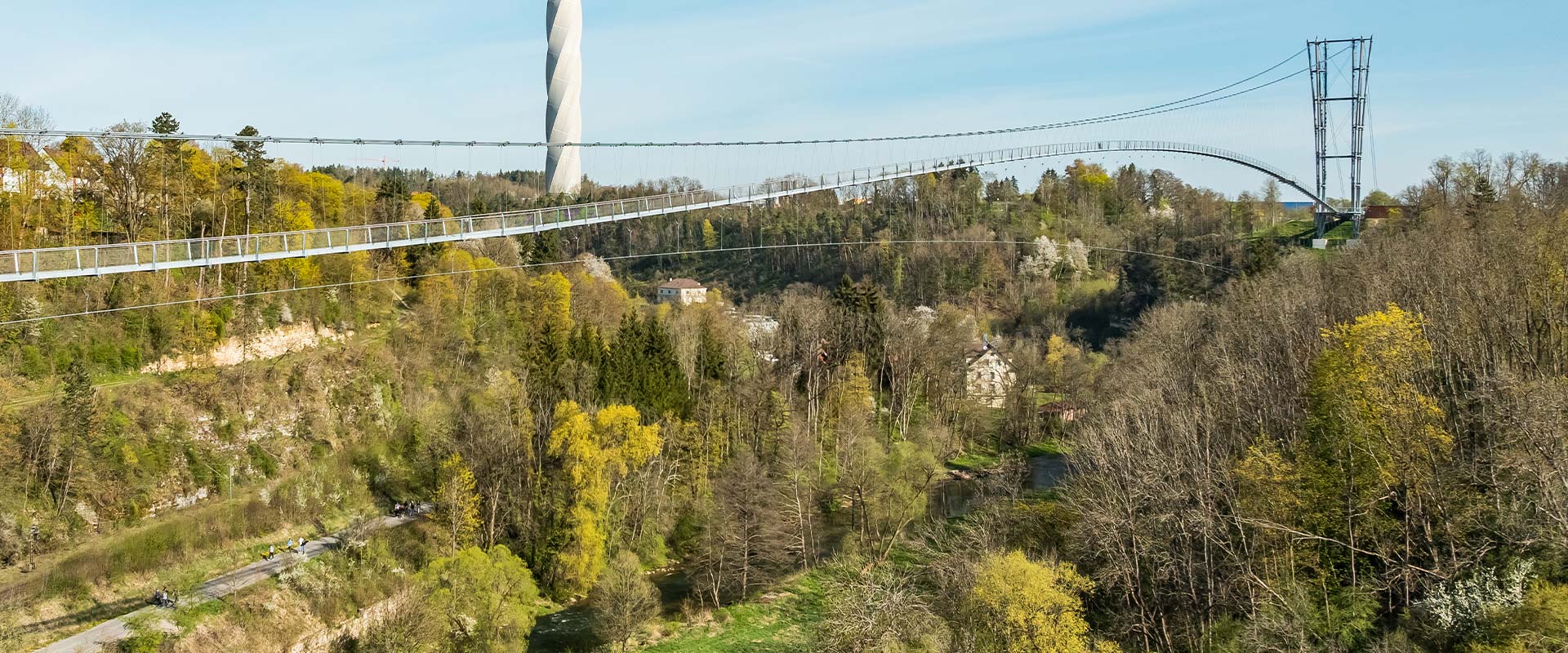 Eine sehr lange Brücke über Baumkronen mit einem futuristischen Turm inmitten von Grün