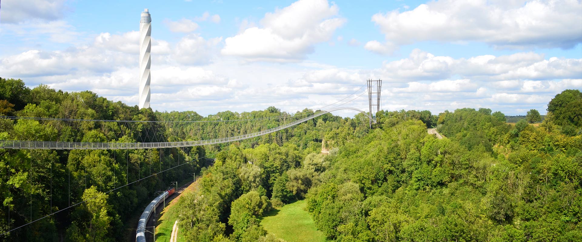 Eine sehr lange Brücke über Baumkronen mit einem futuristischen Turm inmitten von Grün