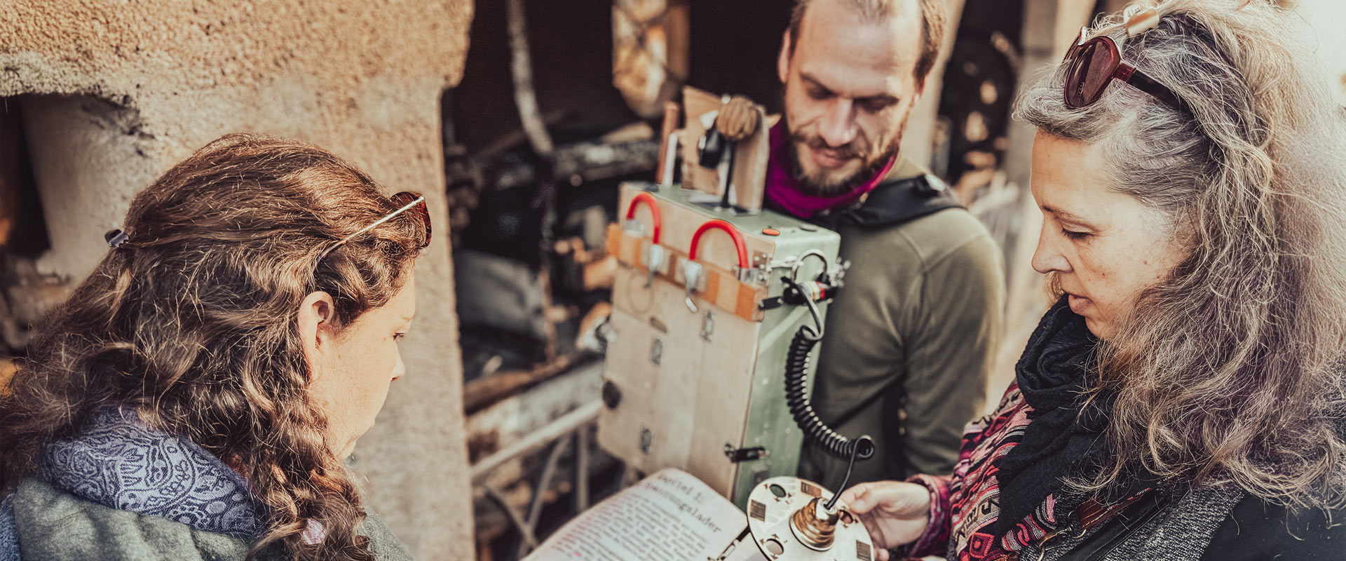 drei Personen blicken auf Gerätschaften zum Rätsellösen an einer Gebäudewand im Sonnenlicht