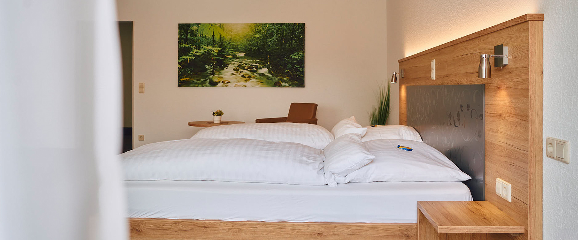 Ansicht auf Doppelbett in geräumigem Zimmer mit Waldbild an der Wand