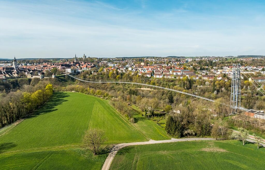 Abbildung einer Hängebrücke mit Altstadt im Hintergrund.